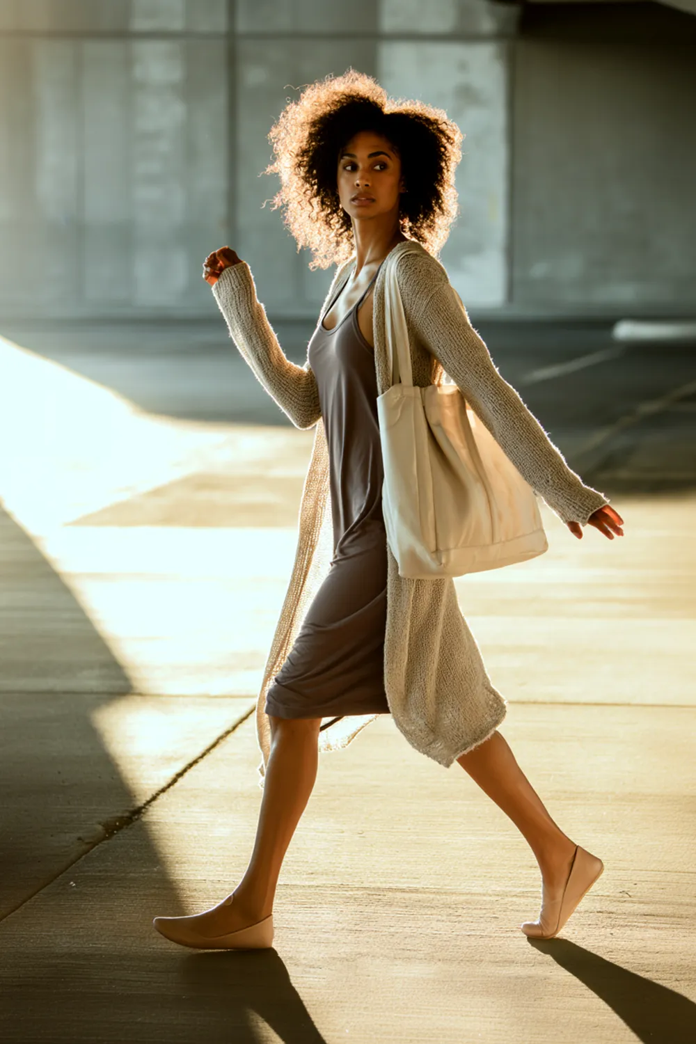 Woman walking outdoors wearing a lightweight open-front cardigan over a sleeveless dress, carrying a tote