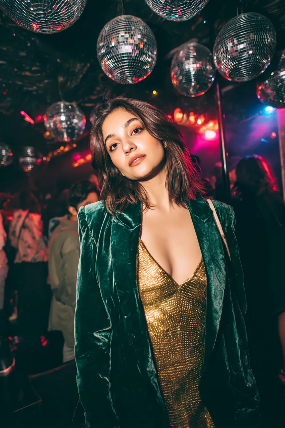 Woman wearing a green velvet blazer and gold sequin dress under disco balls at a New Year’s Eve party