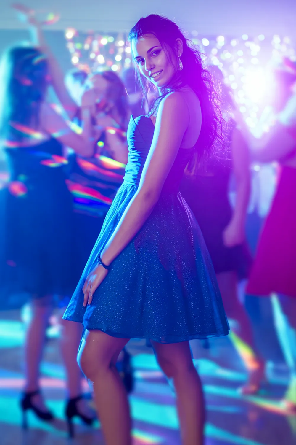 Petite girl in short blue homecoming dress smiling on dance floor with party lights