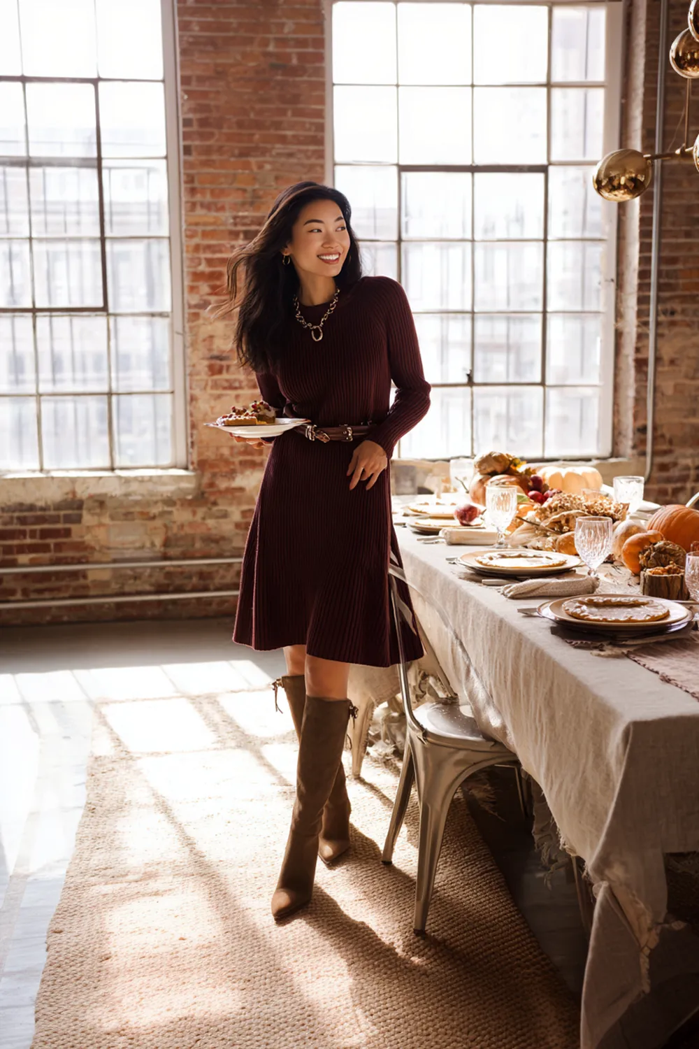 Woman in burgundy knit dress and knee-high boots at a Thanksgiving loft dinner table