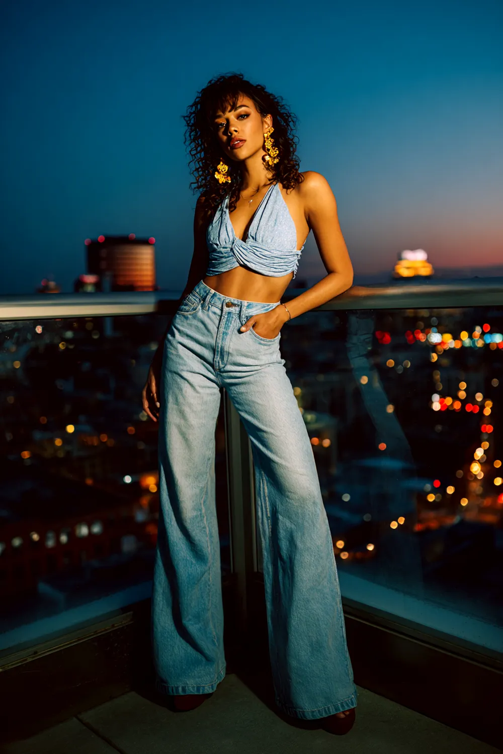 Woman in flared jeans with platform heels and a crop top posing on a rooftop at night in a casual date night outfit
