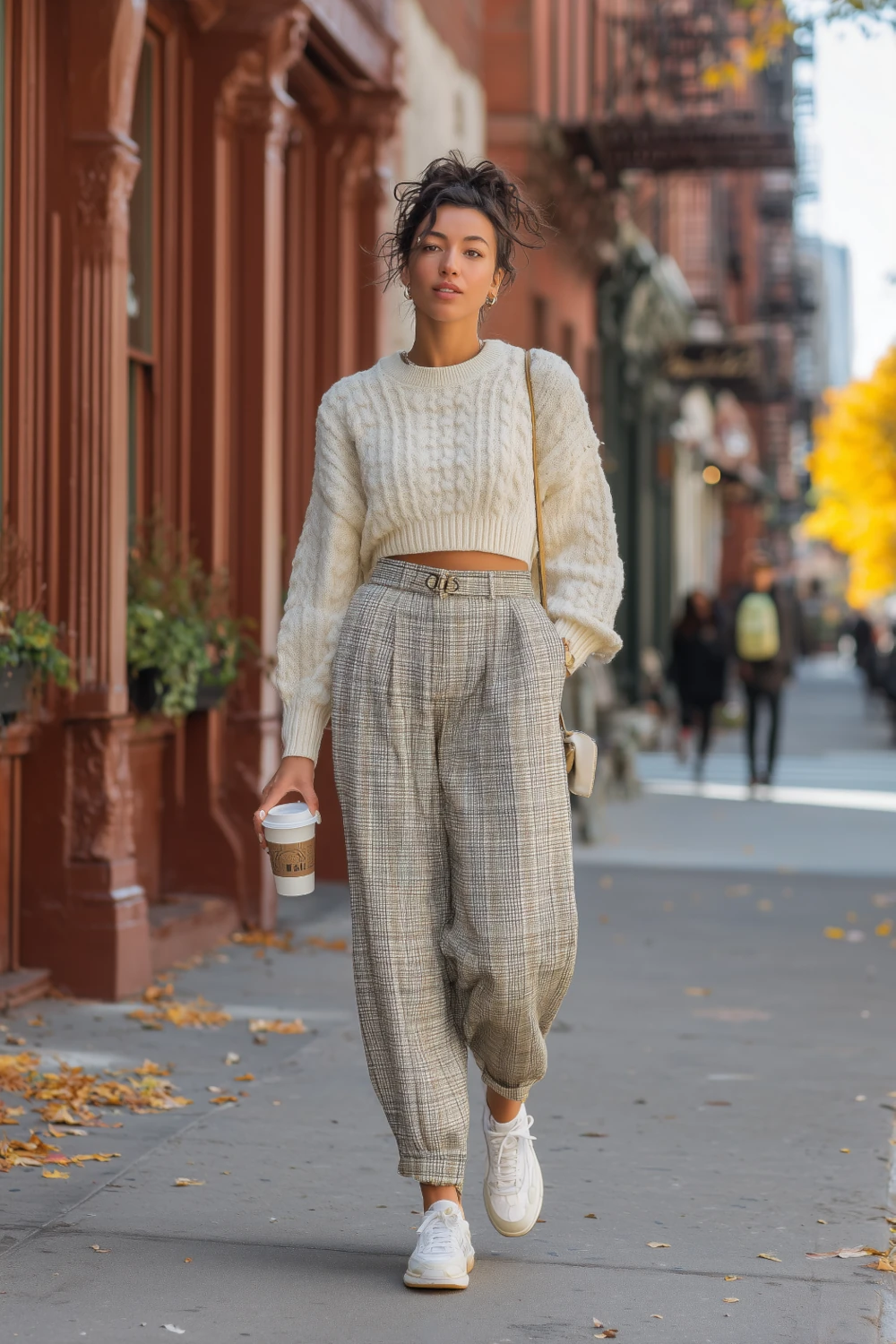 Woman in plaid pants, cropped sweater and white sneakers walking down a city street in fall, casual autumn outfit inspiration